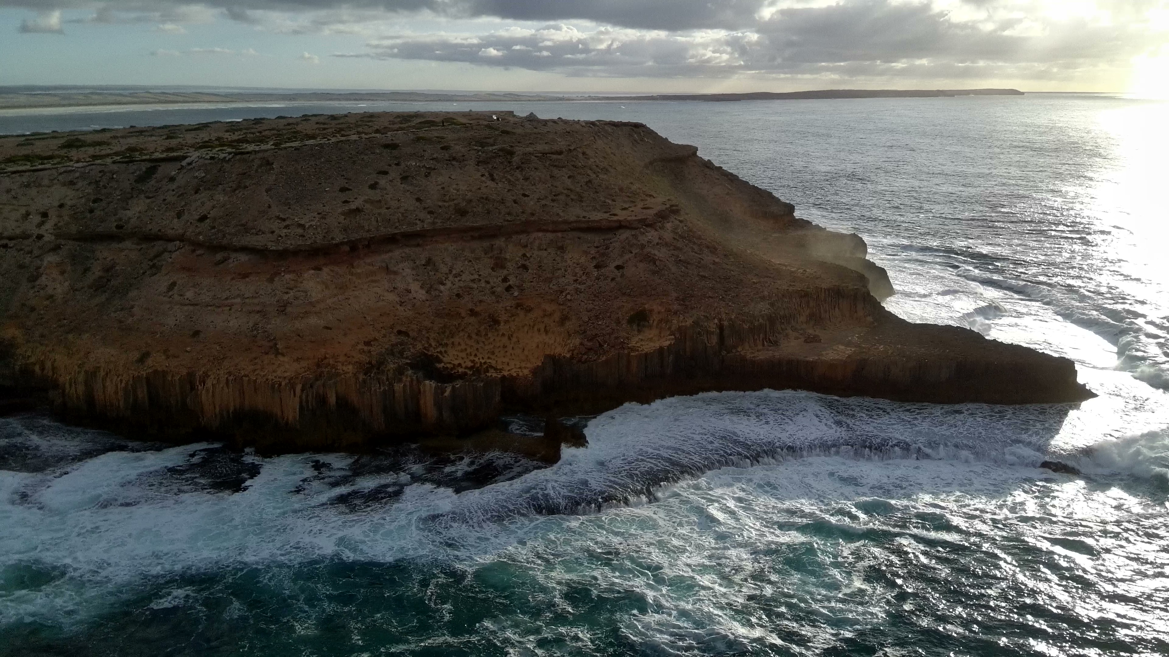 4K aerial drone view across the limestone headland, surrounding turquoise shallows, and ocean breaks.